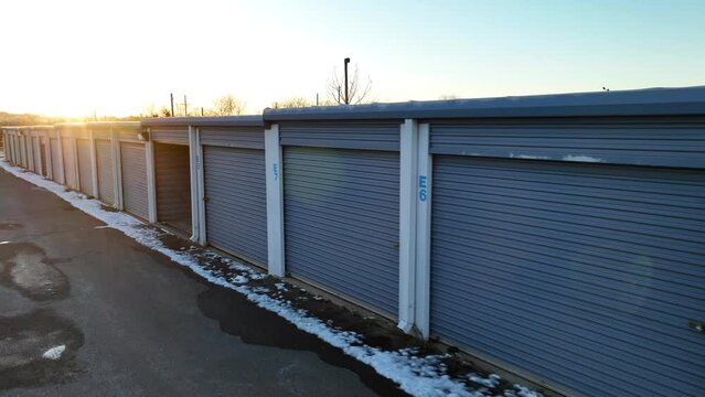 Self storage units with snow during golden hour winter sunset. One open and empty garage unit. Aerial.