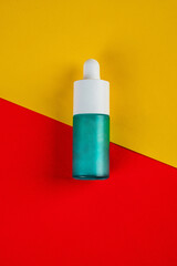 Blue glass cosmetic bottle, Skin care or sunscreen cosmetic on yellow and red background.