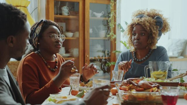 Young African American relatives having conversation when sitting around dinner table with family and eating holiday meal at home