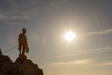 A man is standing on a rock with a rope around his waist. The sun is shining brightly in the...