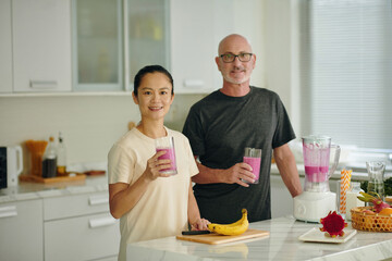 Smiling mature man and woman having pink smoothie for breakfast - 786829468