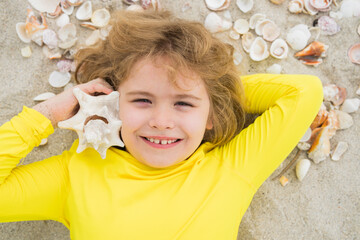 Kid laying on sandy beach with Shells. Summer kids. Summer, beach and vacation concept. Top view of child rest on sand. Child play with Sea shells and fine beach sand. - 786830825