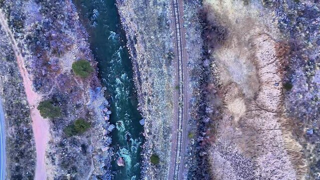 Vertical, aerial footage of a moody dawn in a mountain canyon.  The Arkansas River flows next to abandoned rail road tracks.
