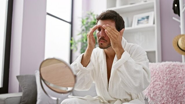 Young handsome man in white robe grooming face indoors