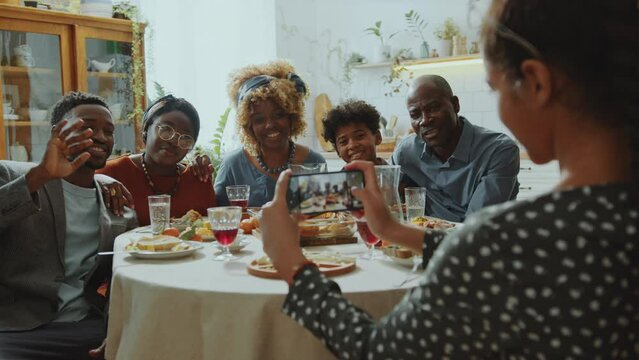 Joyous Black family smiling and posing together for group photo taken by girl with mobile phone during holiday dinner at home