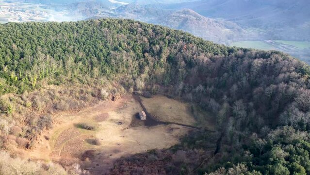 Aerial Drone Slow Helix Circle Around the Inactive Santa Margarida Volcano: Massive Crater and Historic Chapel in Catalonia Spain. Chapel in Overgrown Forested Ruins in the Pyrenees Mountain Ranges.