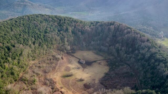 Aerial Slow Circle Around the Inactive Santa Margarida Volcano: Massive Crater and Historic Chapel in Catalonia Spain. Overgrown Forested Ruins in the Pyrenees Mountain Ranges. 4K