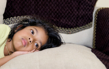 little asian girl sadly lying on the sofa in the living room at home
