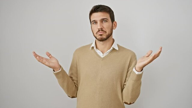 Portrait of a clueless young hispanic man, wearing sweater, standing with hands raised in a puzzled 'i don't know' gesture against a white, isolated background. emotive expression of doubt.