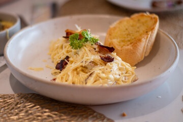 Carbonara pasta with pancetta, egg, hard parmesan cheese and cream sauce. White plate on white wooden background.
