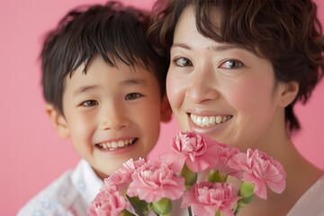 A carnations bouquet in front of the face, a smiling Japanese boy and his mother holding carnation flowers on a pink background for a Mother's Day celebration, in a studio shot.