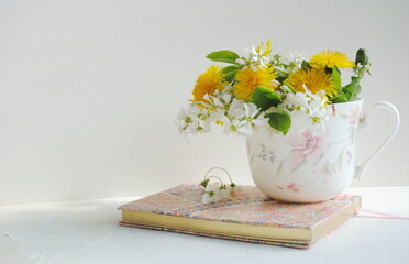 White flowers and yellow dandelion flowers in a cup on a white background. Postcard, place for text.