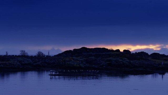 Twilight. Seagulls resting on an abandoned fish farm cage by the small island connected breakwater. Lofoten Islands, Northern Norway.