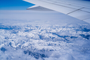 Aerial view through porthole of plane to of snow-covered mountain. Scenic view through aircraft....