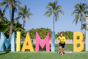Kid near Miami Beach sign. Kid enjoy summer vacation holiday. Travel, childhood happiness concept. Summer Holiday at Miami Beach Florida. Blond little kid boy having fun on Miami beach, Ocean drive. - 786861008