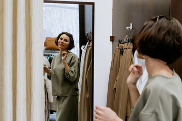Happy woman tries on clothes while looking at herself in the mirror in the locker room, posing, shopping for casual clothes, in fashionable women's clothing store, in boutique. Shopping.