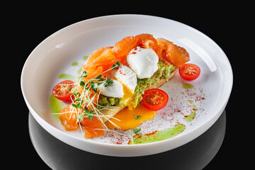 poached egg toast with avocado and salmon on a white plate