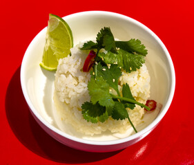 Rice in a plate with lemon and herbs on a red background