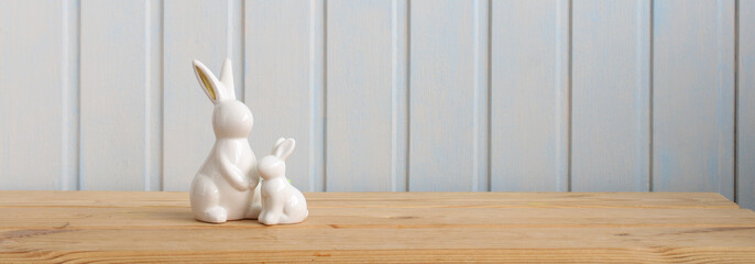 Easter banner with Easter bunny figurines on a table on a white board background. Festive long...