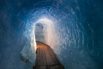 Amazing blue ice tunnel for tourists inside of Rhone glacier. Fantastic view of ice wall and wooden pathway in glacier of Swiss Alps, Bern canton, Switzerland, Europe. Traveling concept background.
