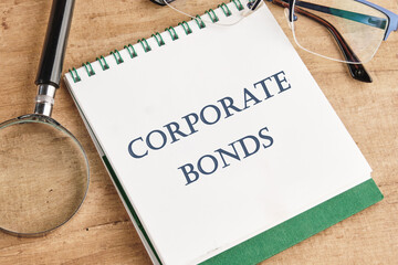 Finance and economics concept. CORPORATE BONDS written on a notebook with a magnifying glass and glasses on a vintage background - obrazy, fototapety, plakaty