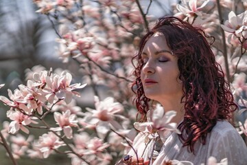 Magnolia park woman. Stylish woman in a hat stands near the magnolia bush in the park. Dressed in...