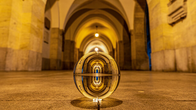 Historische Minoritenkirche in Wien bei Nacht, hell erleuchteter Arkadengang in goldenem Licht spiegelt sich in Glaskugel