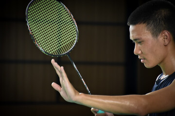 A male badminton player holds a racket in right hand and raises left hand forward to signal his opponent that he is not ready to receive the serve from his opponent in a badminton men's single match.