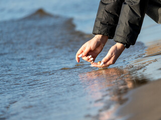 The hands of a woman looking for shells in the sand on the seafront.