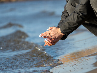 The hands of a woman looking for shells in the sand on the seafront.