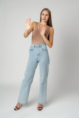 Young Woman in Fashionable Outfit Standing Against a Neutral Backdrop Showing Stop Gesture