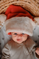 The newborn is lying in a cradle, wearing a Santa Claus hat.
