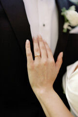Bride's hand with engagement ring against groom's suit