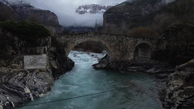 Drone shot of a bridge over a river in a mountainous area