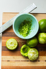 Zested and halved limes on a striped cutting board