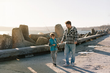A young father with a small toddler son outdoors fishing by a sea