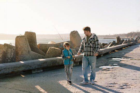 A young father with a small toddler son outdoors fishing by a sea