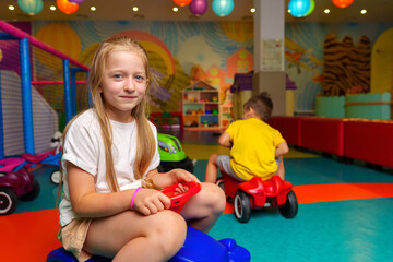 Young Girl Sitting on Toy Car in Play Room