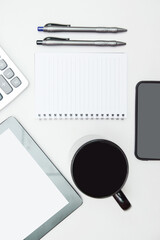 White office desk table with blank notebook, tablet, mobile phone, calculator, a cup of coffee and other office supplies. Top view with copy space, flat lay.