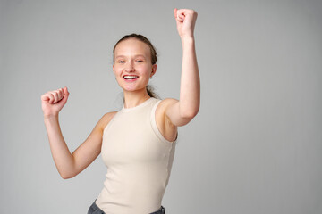 Young Woman in Casual Attire Smiling and Making a Fist Pump Gesture on a Plain Background