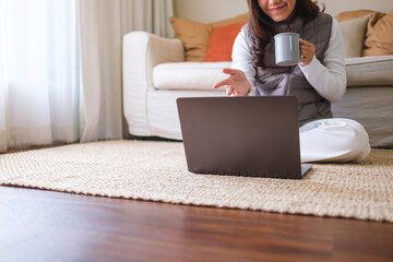 Closeup of a young woman drinking coffee while using laptop computer for video call at home - 786900065