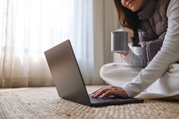 Closeup image of a young woman drinking coffee while working on laptop computer at home - 786900237