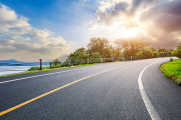 Asphalt highway road and green trees with sky clouds landscape at sunset