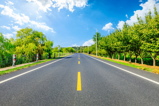 Straight asphalt road and green forest with sky clouds natural landscape on a sunny day