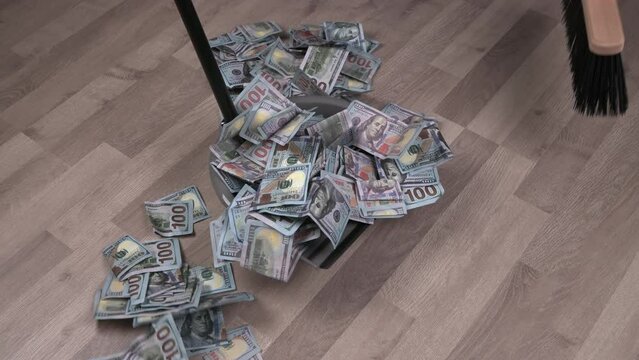 Broom sweeps heap of dollar banknotes in dustpan on wooden floor background. Concept of depreciation of money high inflation.