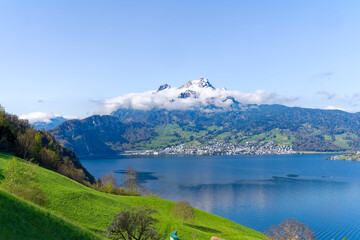 Scenic rural landscape with Lake Lucerne and snow covered mountains in the background seen from Swiss village Kehrsiten on a sunny spring day. Photo taken April 11th, 2024, Kehrsiten, Switzerland.
