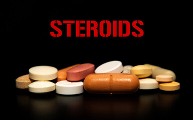 A pile of medication pills on a black background with the inscription STEROIDS