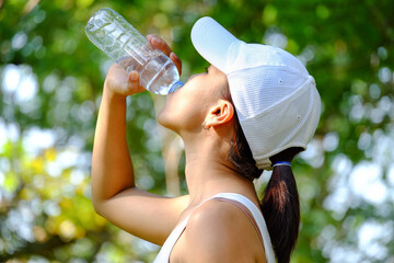 Female athlete lifts a bottle of drinking water in a clean bottle in hot weather with very sunny natural green background. Health and hydration concepts