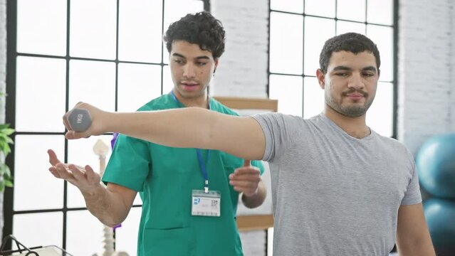 Therapist assisting patient with dumbbell exercise in a bright physiotherapy clinic, showcasing healthcare and rehabilitation.