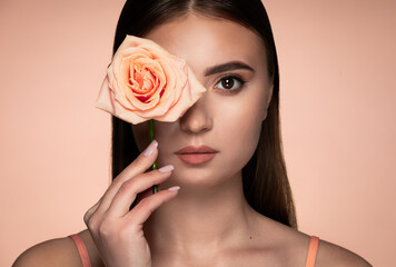 Beauty studio portrait of young beautiful woman holding rose against background in peach tones.